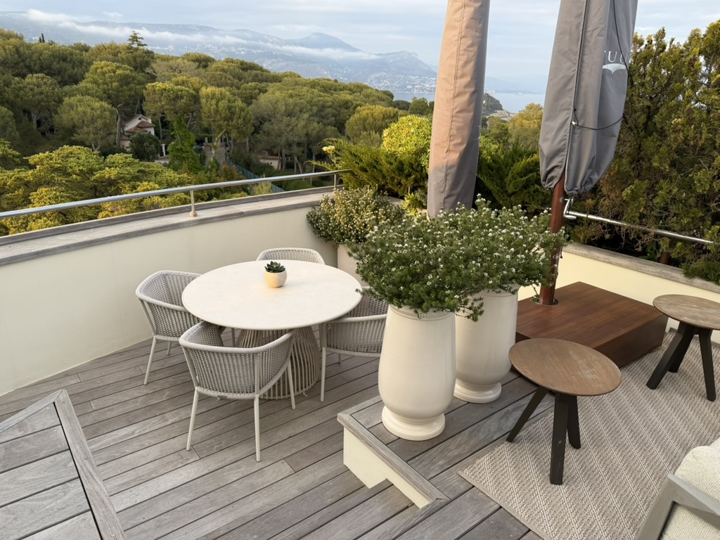 The rooftop terrace at golden hour, mountains behind, Monaco on the horizon